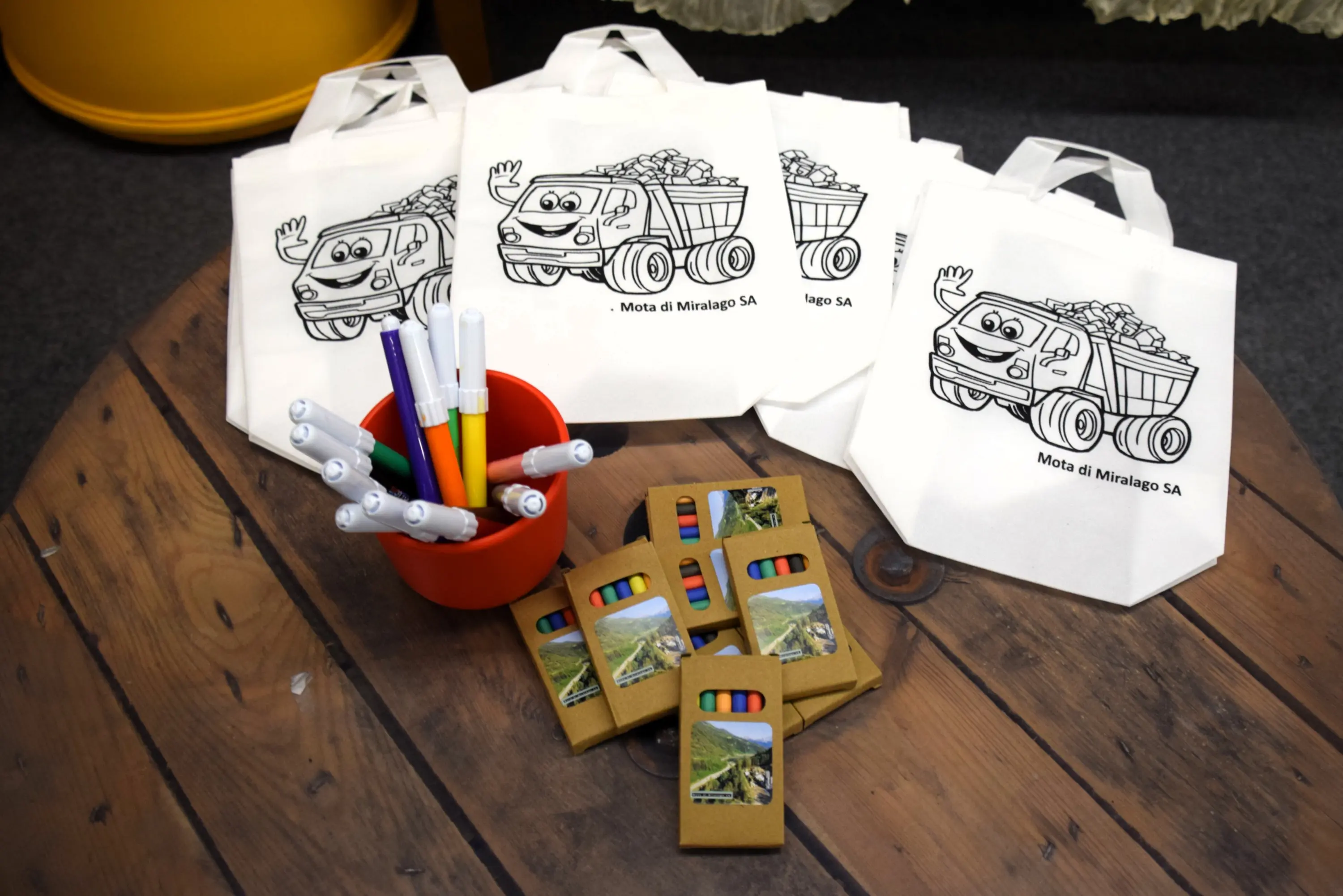 Borse di stoffa stampate con un camioncino e un contenitore di pennarelli colorati, insieme a piccoli quaderni in cartone decorati.