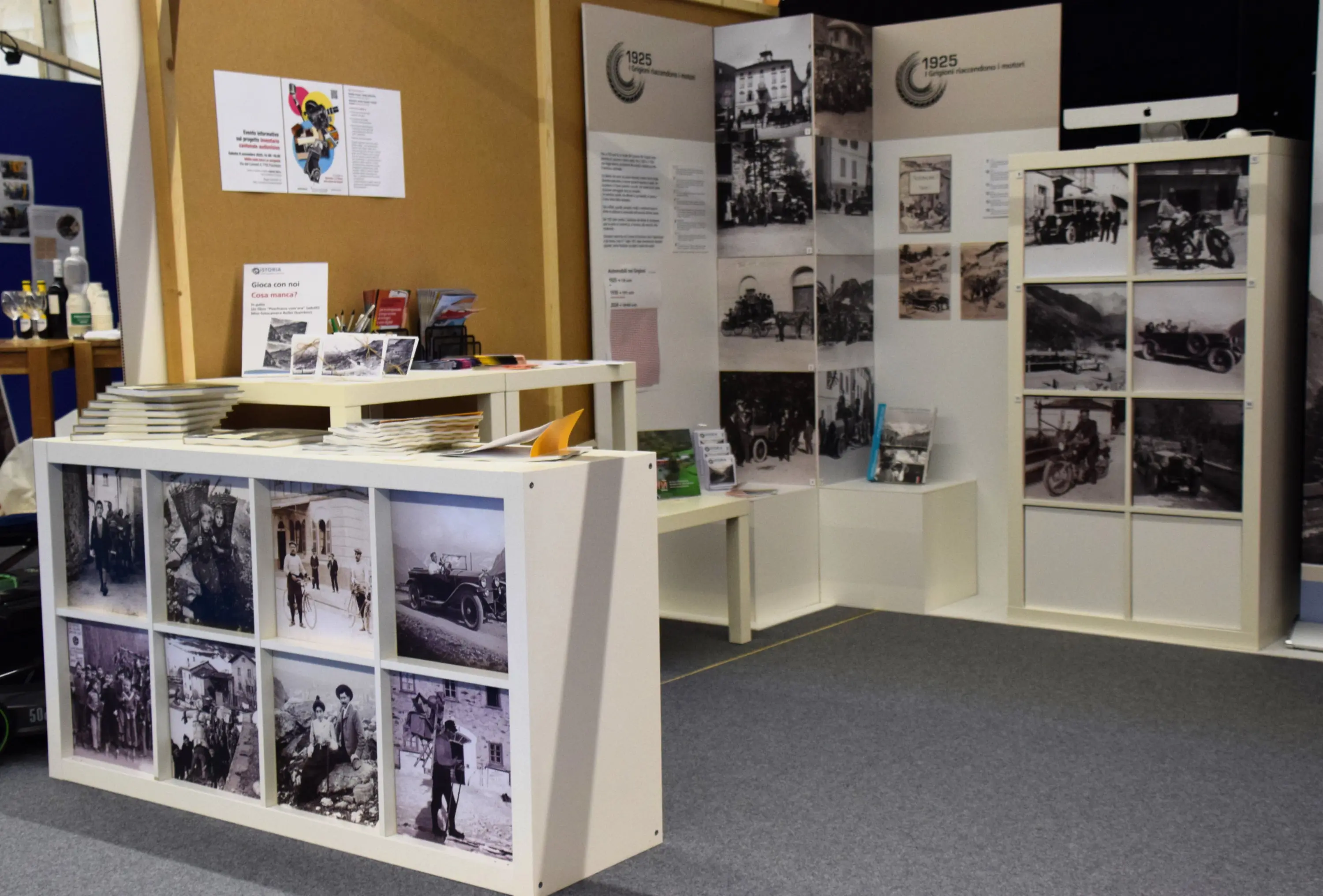 Uno stand espositivo con pannelli informativi e fotografie storiche, inclusi immagini di automobili d'epoca, su uno sfondo neutro. Una zona di accoglienza è visibile con brochure e materiali informativi.