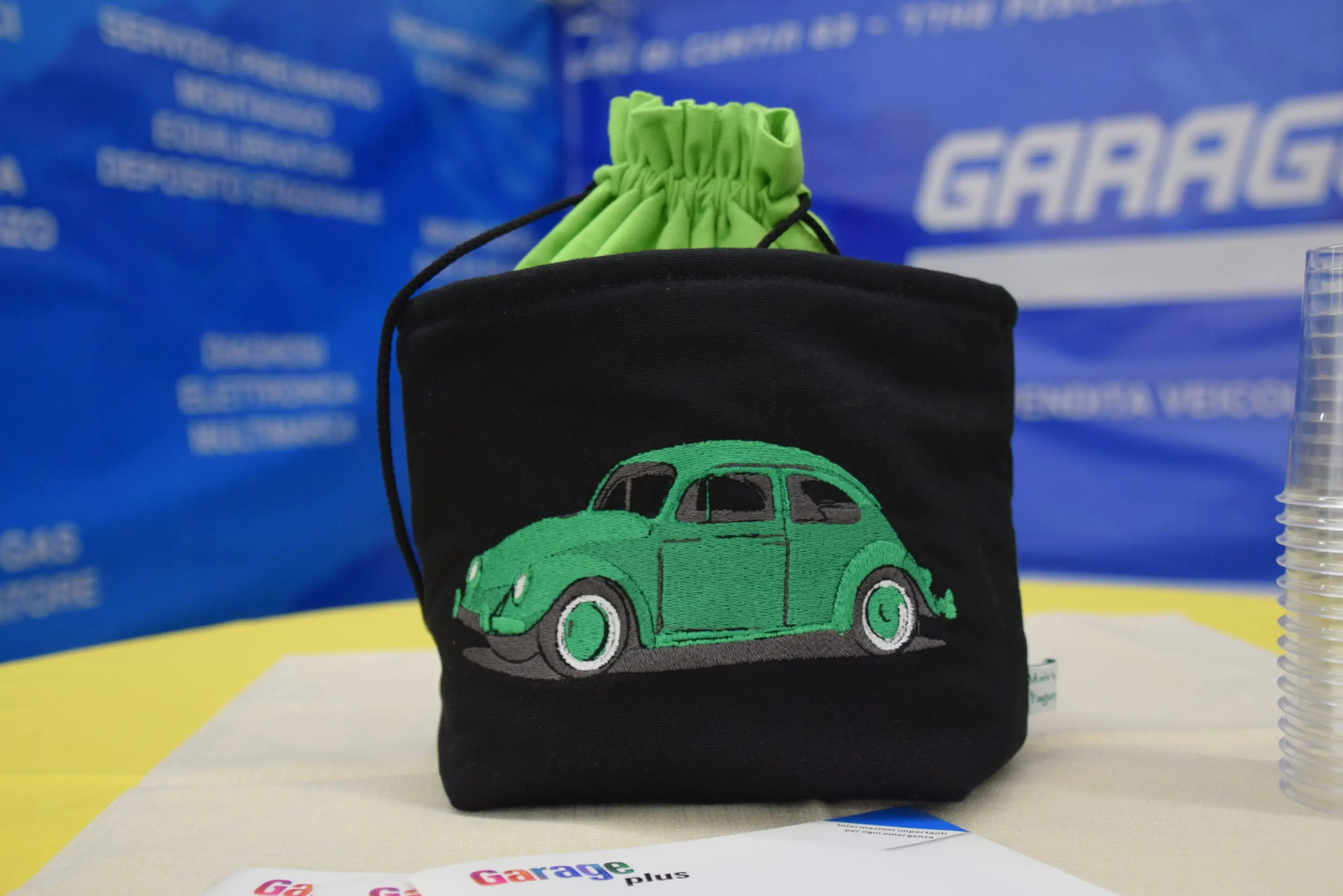 Borsa nera con ricamo di un'auto verde, posizionata su un tavolo giallo con sfondo blu.