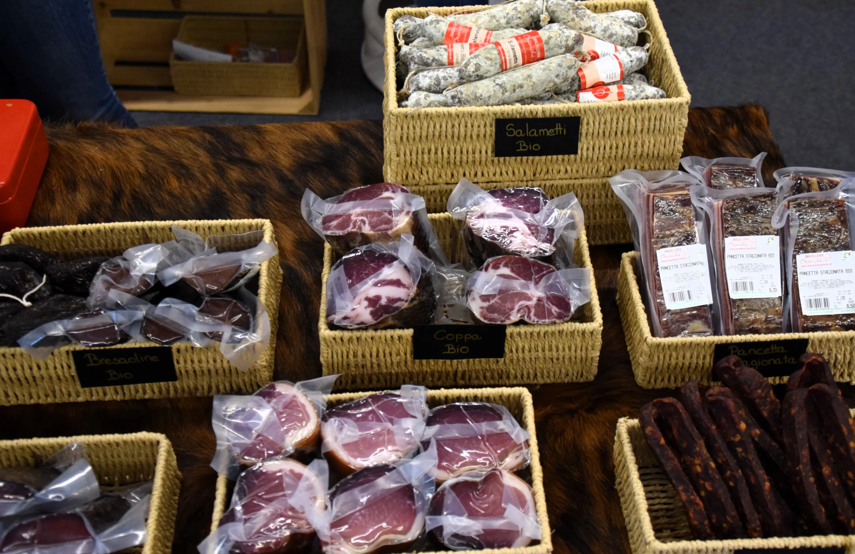 Varie tipologie di salumi disposte in cesti di vimini. Sono presenti salami, coppa e pancetta, tutti etichettati come biologici.