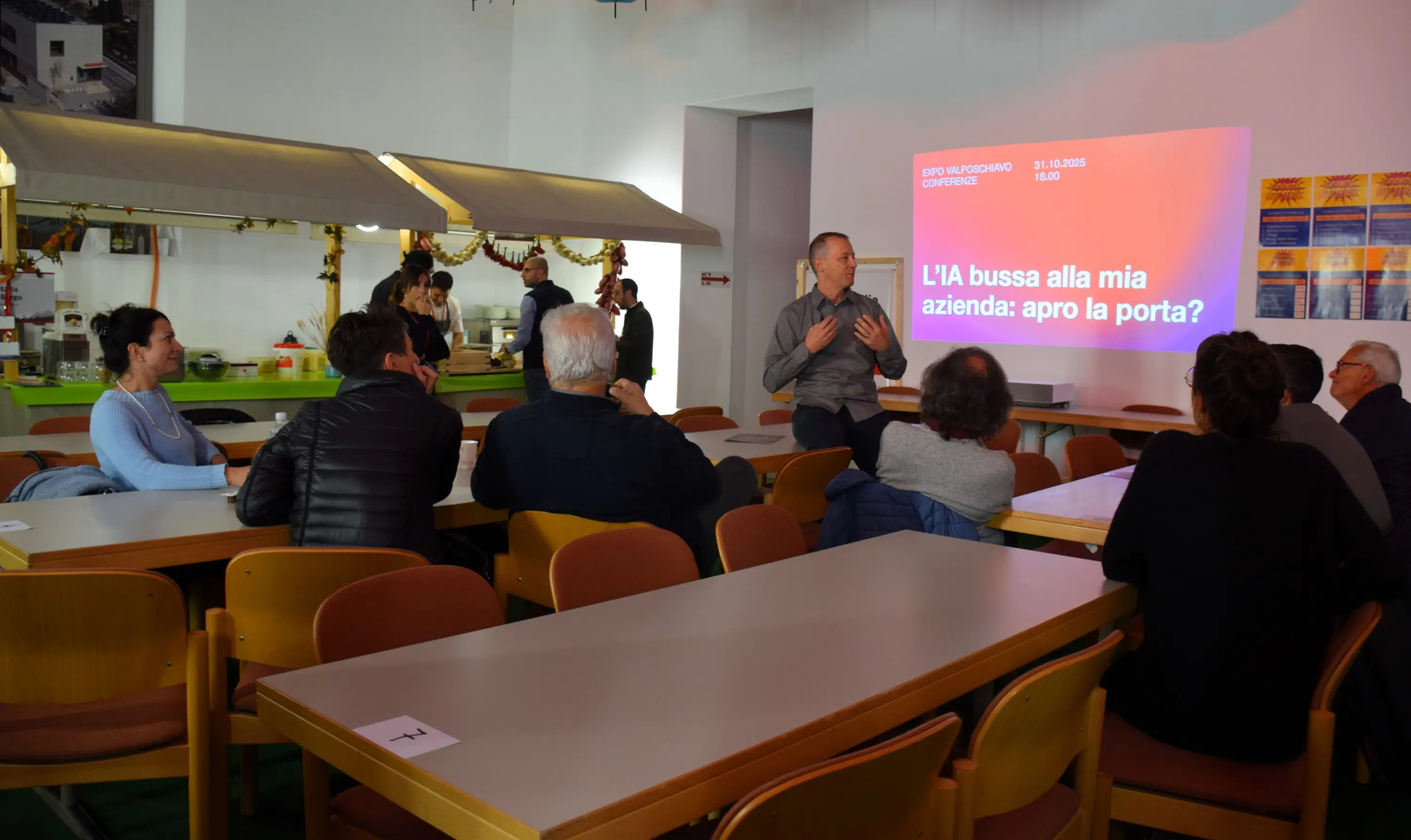 Un relatore sta parlando a un pubblico seduto in una sala luminosa, con un poster di presentazione proiettato sullo sfondo. I partecipanti sembrano interessati e attentamente ascoltano.