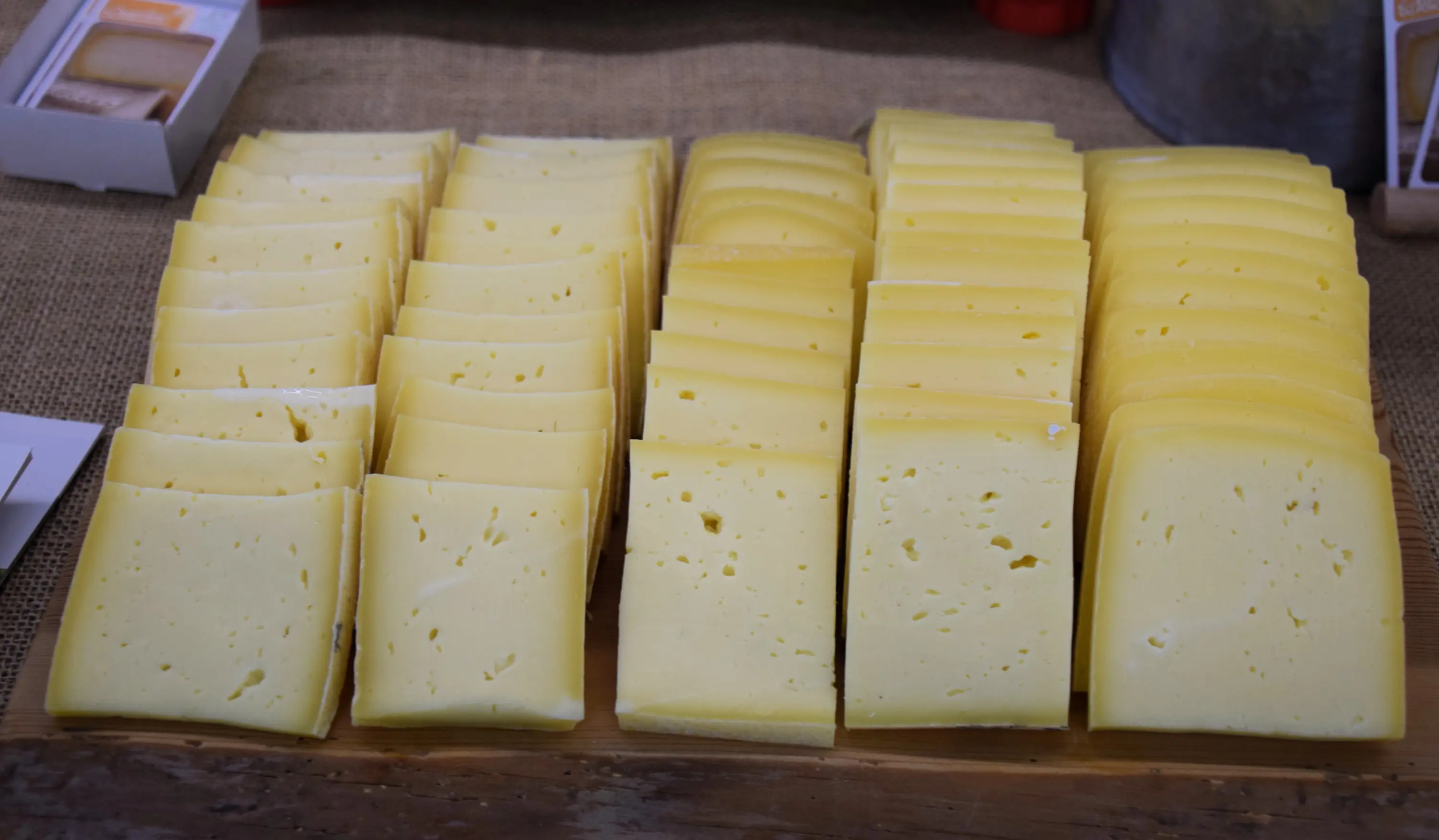 Fette di formaggio giallo disposte ordinatamente su un vassoio di legno.