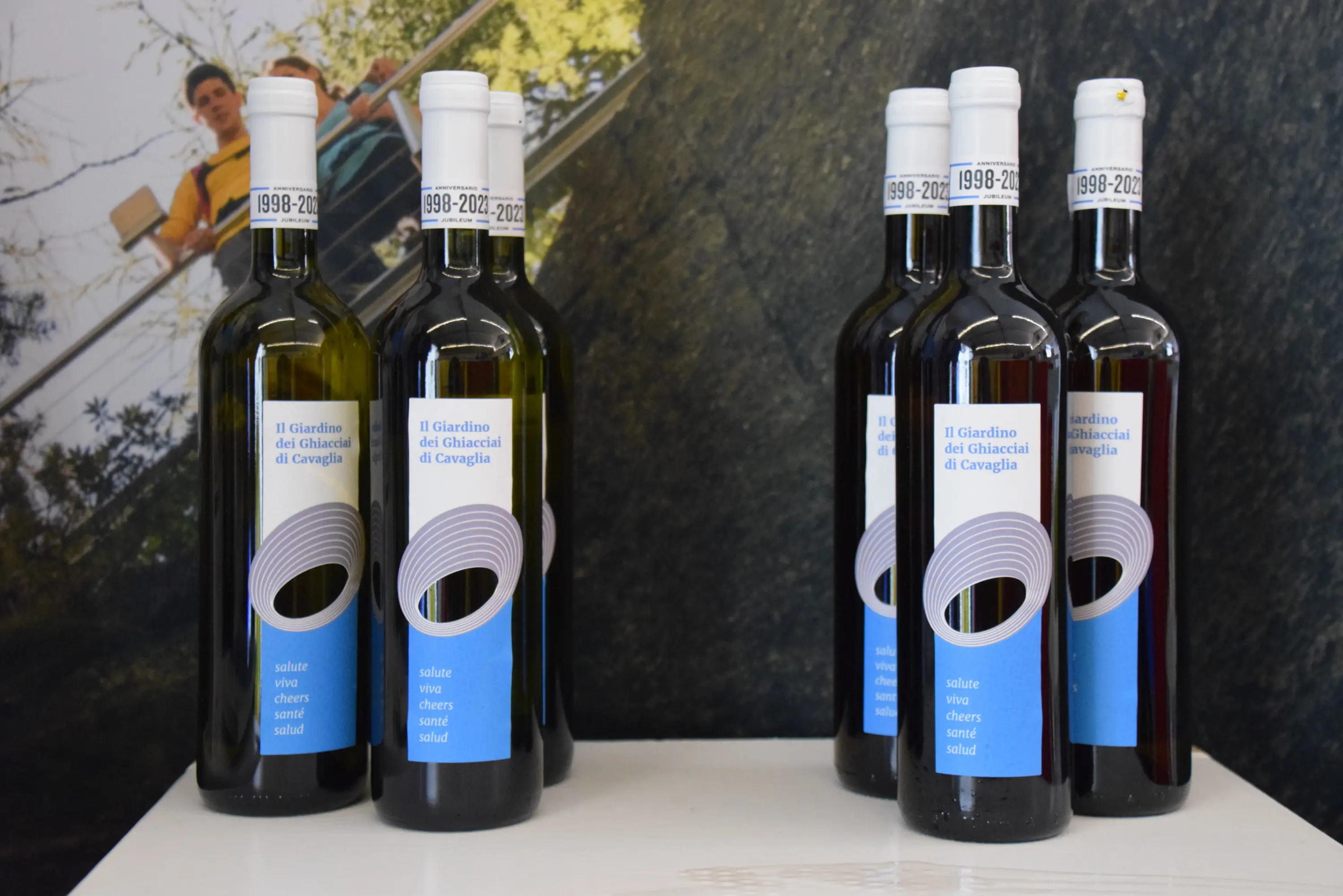 Due gruppi di bottiglie di vino con etichette blu. Le etichette mostrano il nome "Il Giardino dei Cinque Cieli di Cravaglia" e un'immagine stilizzata di un cerchio. Sfondo naturale con vegetazione.