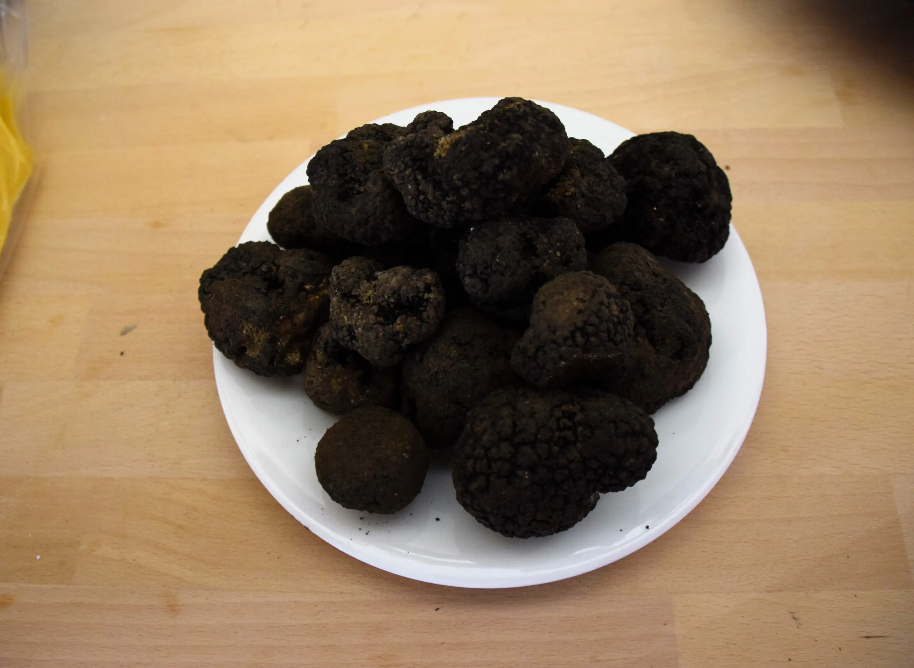 Un piatto bianco con un mucchio di tartufi neri, di diverse dimensioni e forme, con una superficie irregolare e rugosa.