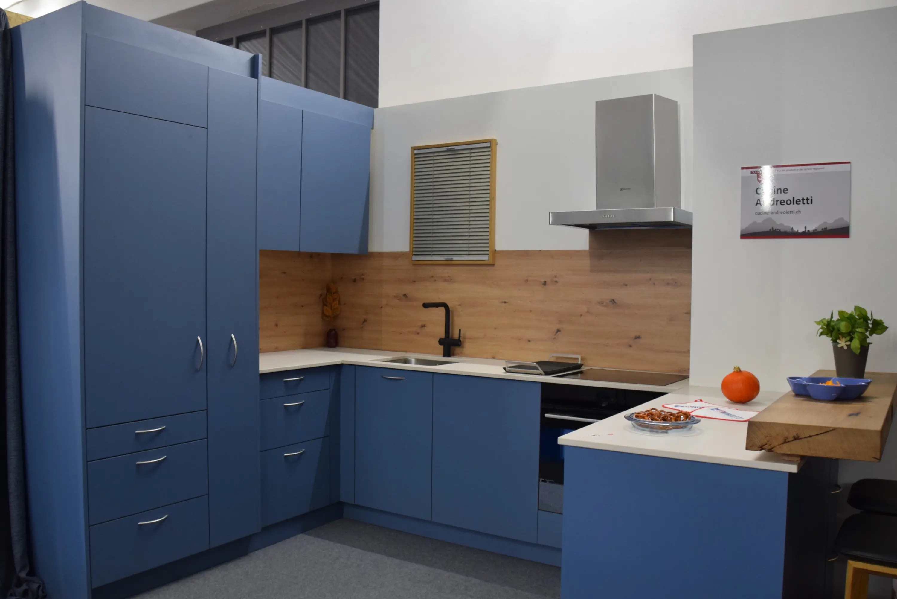 Cucina moderna con mobili blu e una parete in legno. Stufa a gas e lavello neri. Tavolo con un'arancia e un piatto di dolcetti. Atmosfera accogliente e contemporanea.