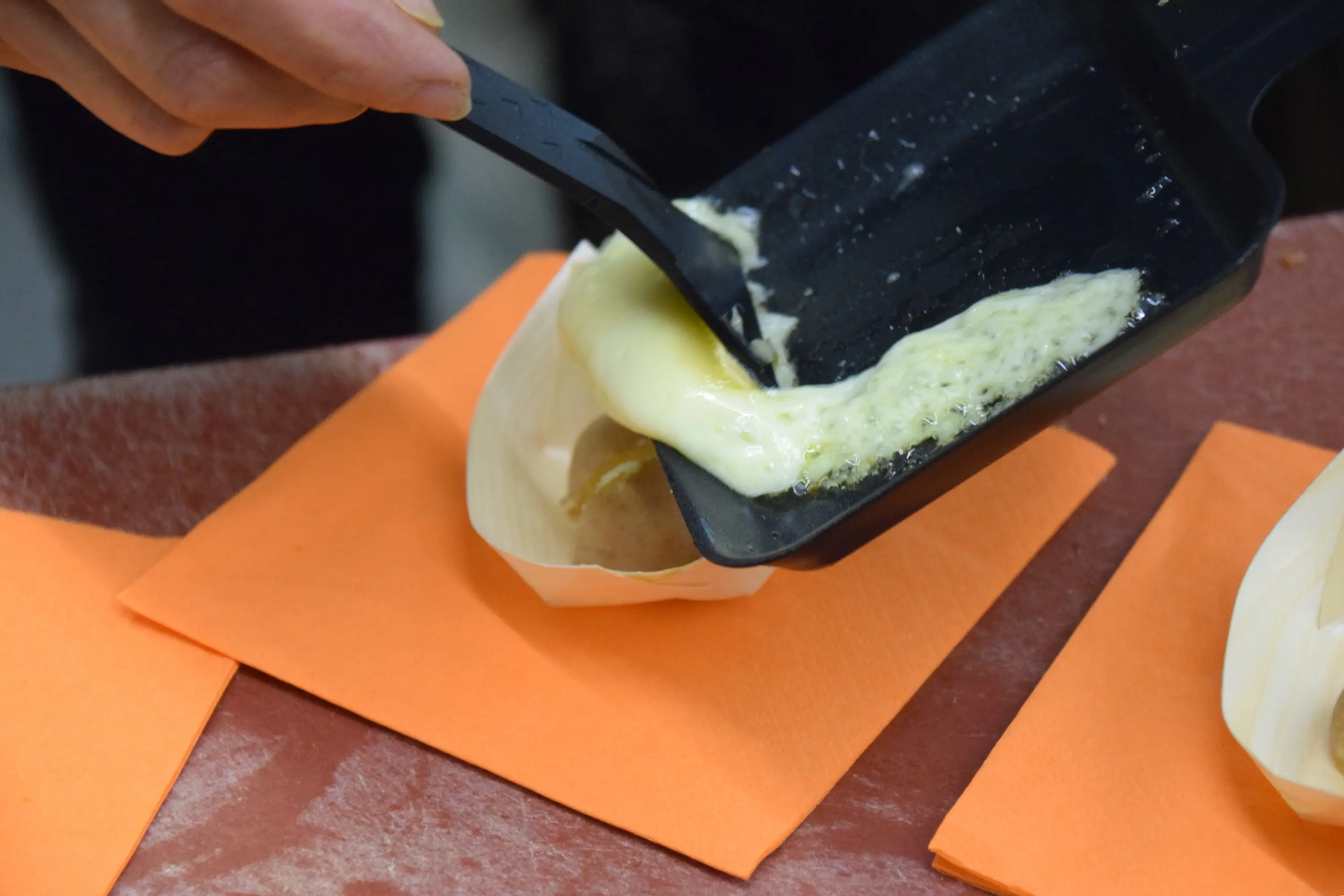 Una mano utilizza una paletta di plastica per servire una porzione di formaggio fuso su un piatto arancione.