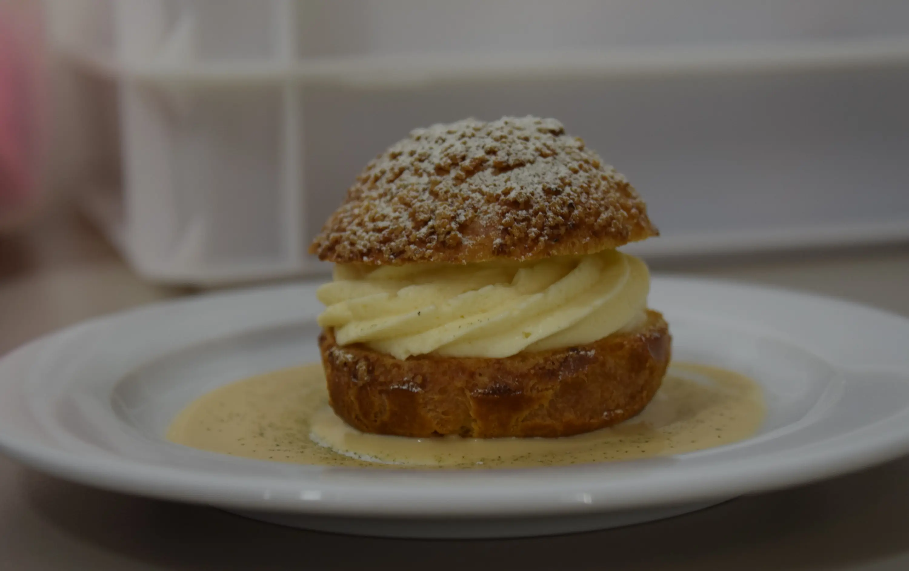 Un dolce a base di pasta choux con una soffice crema al burro, spolverato di zucchero a velo e adagiato su una salsa chiara.