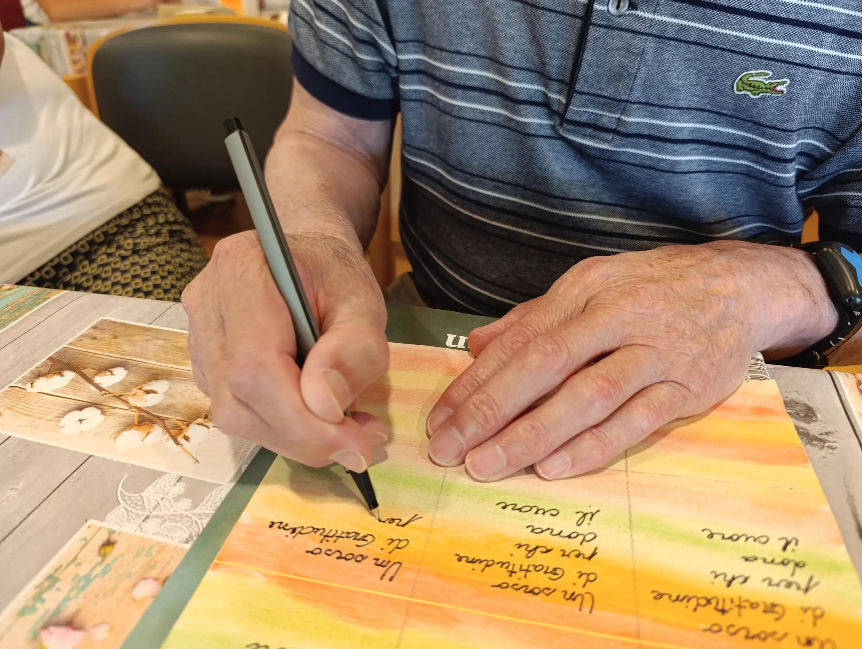 Una persona sta scrivendo con una penna su un foglio colorato. Si vedono le mani ben in vista, con una maglietta a righe.