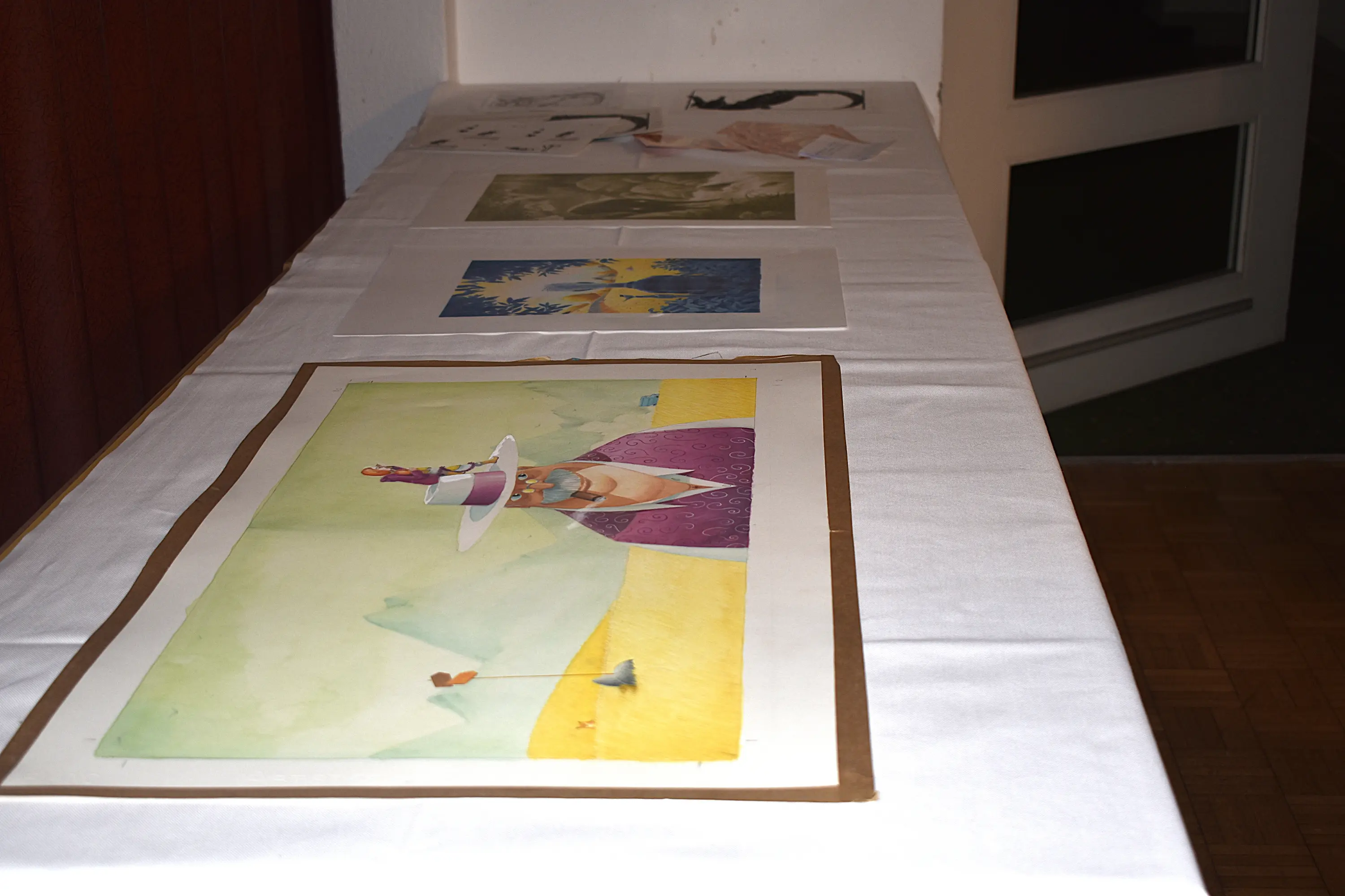 Illustrazioni colorate su un tavolo, con una figura in un cappello bianco al centro, circondata da altri disegni.