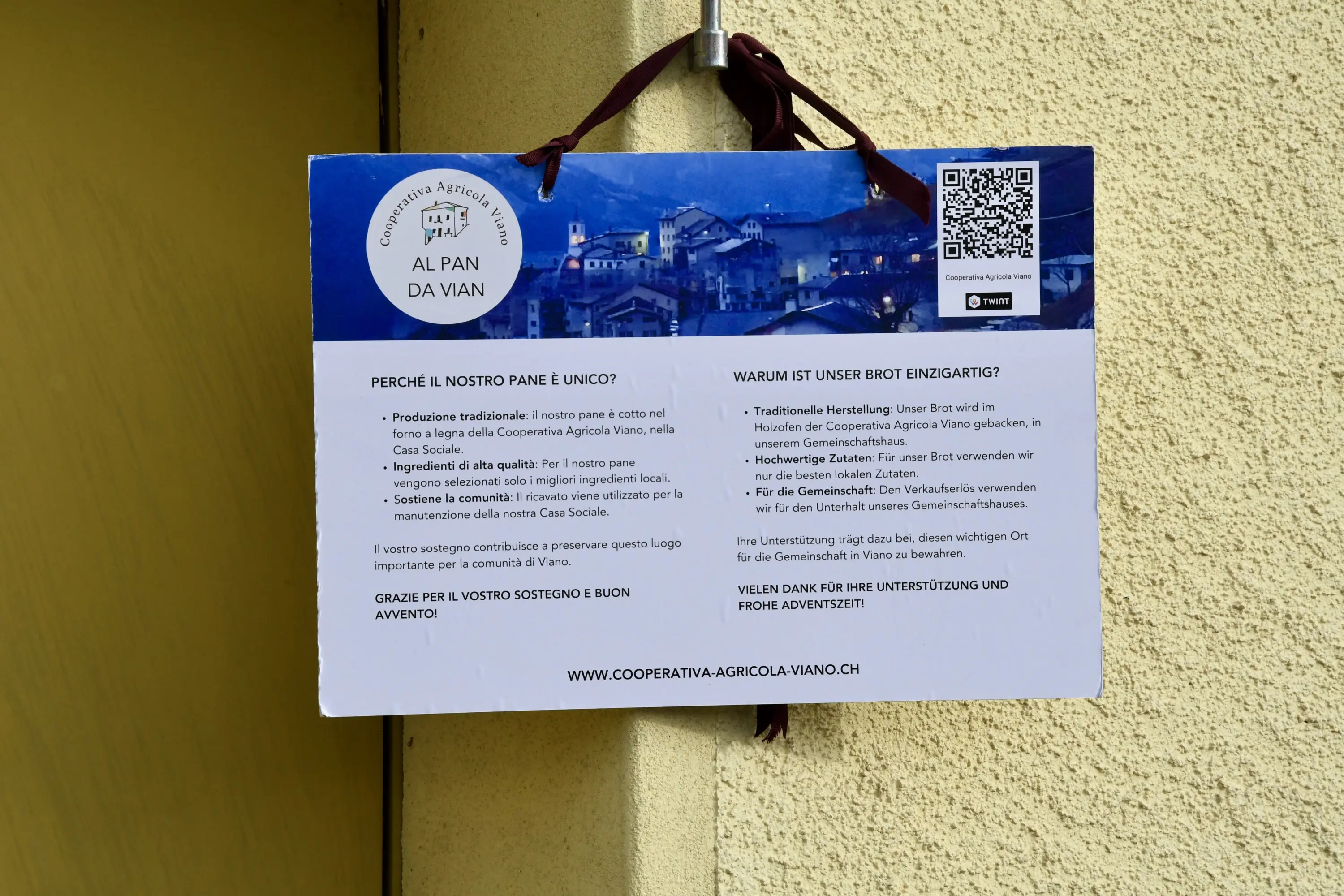 Cartello affisso a una porta con informazioni sulla produzione tradizionale di pane, includendo motivazioni e dettagli sulla cooperativa agricola Al Pan di Vian. Contiene testo in italiano e