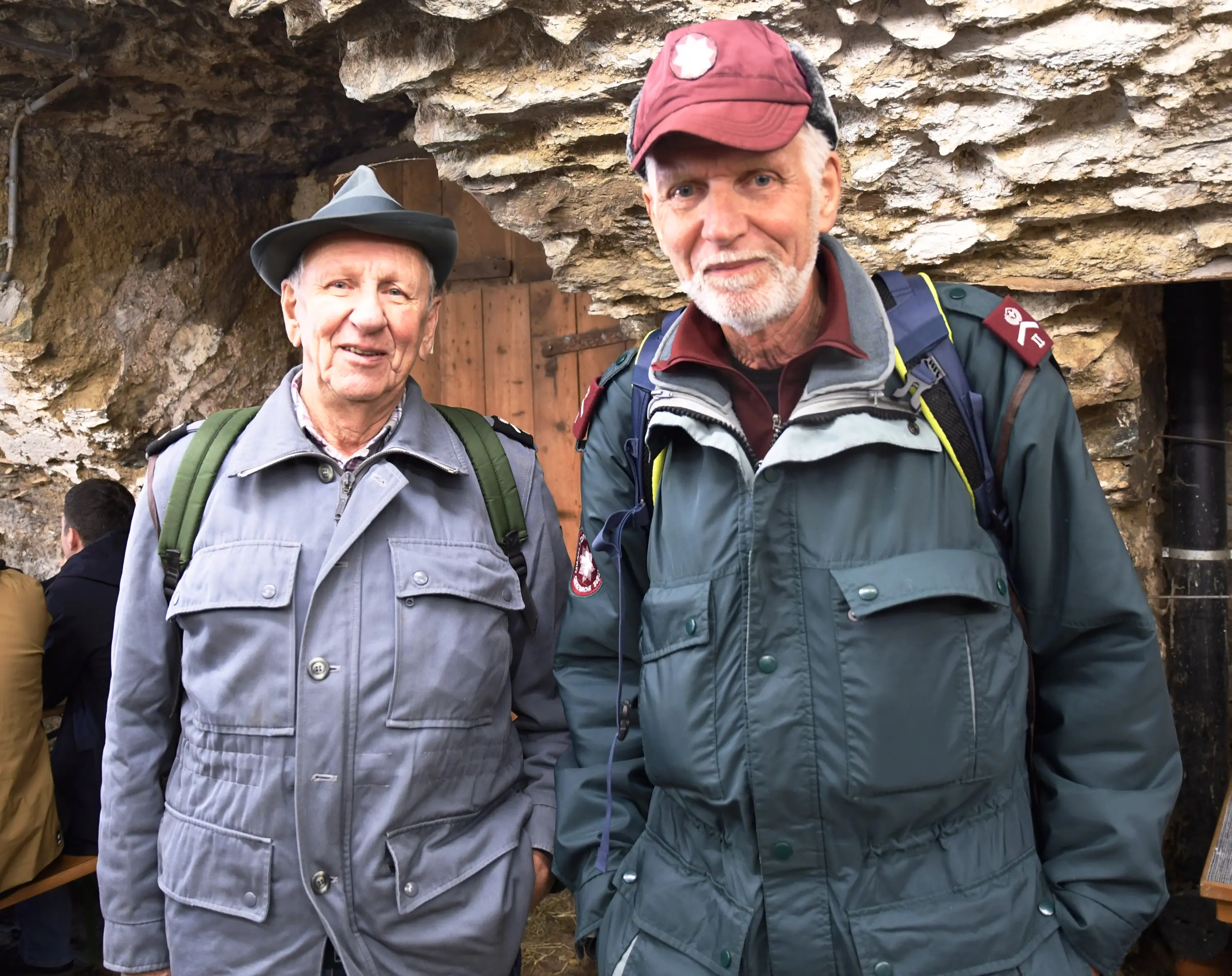 Due uomini sorridenti in abbigliamento da escursionismo, uno con un cappello grigio e l'altro con un cappellino maroon. Si trovano all’interno di
