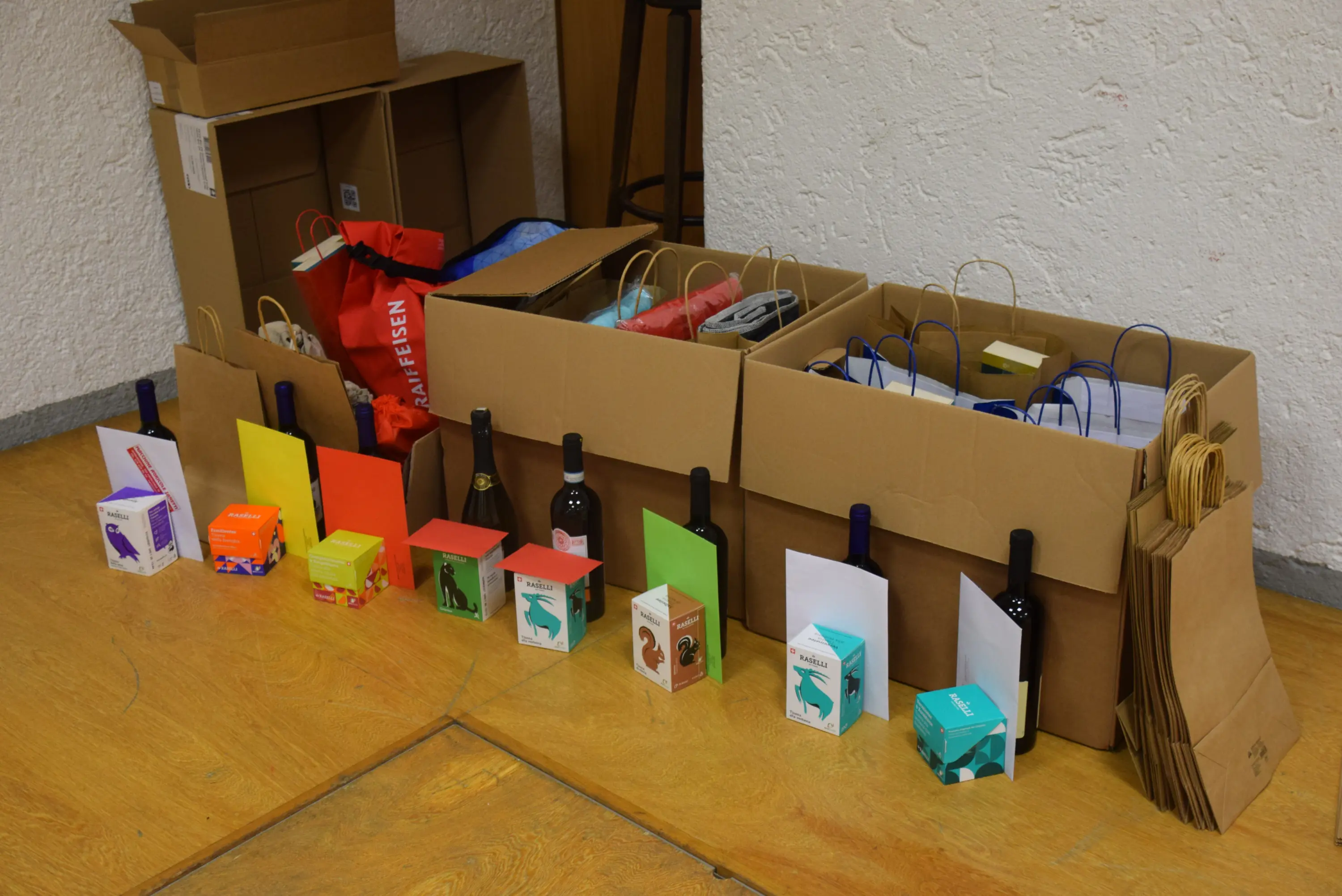 Vari scatole di cartone piene di regali e contenitori colorati, con bottiglie di vino in mostra. Alcuni sacchetti di carta sono disposti accanto ai pacchi.