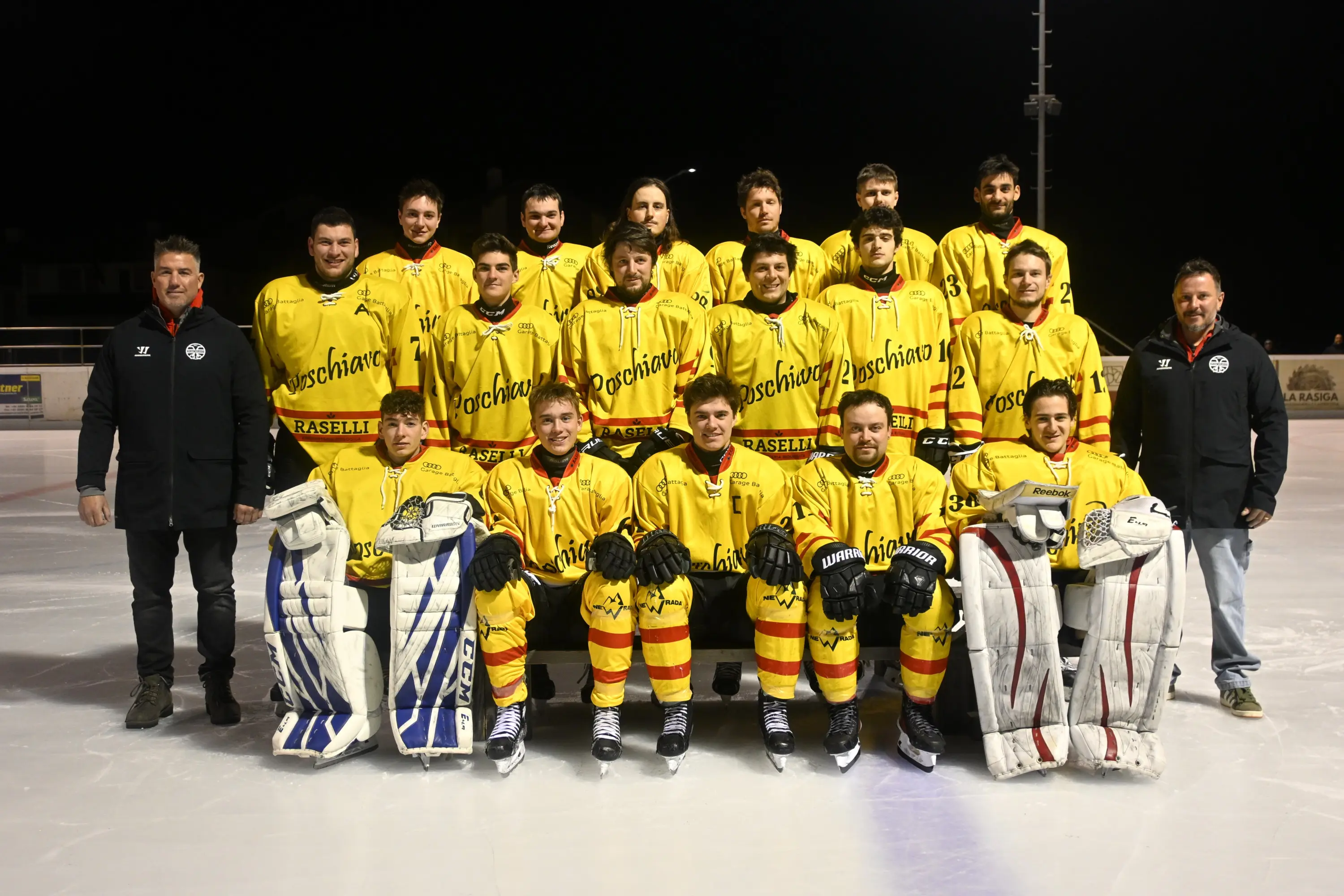 Squadra di hockey su ghiaccio in divisa gialla, composta da giocatori e allenatori. Sono in posa su un campo di ghiaccio, con il portiere in primo piano.