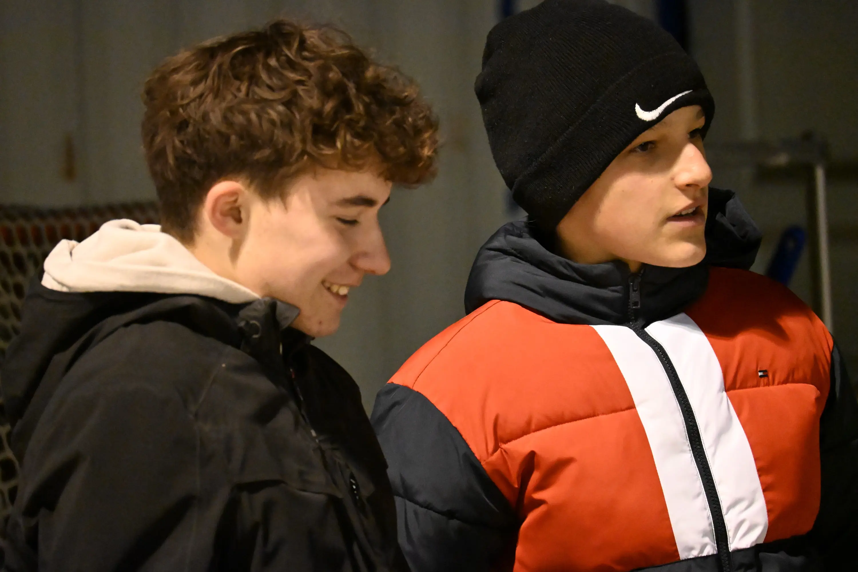 Due ragazzi sorridono mentre discutono. Uno indossa una giacca nera e l'altro una giacca colorata con strisce bianche e rosse.