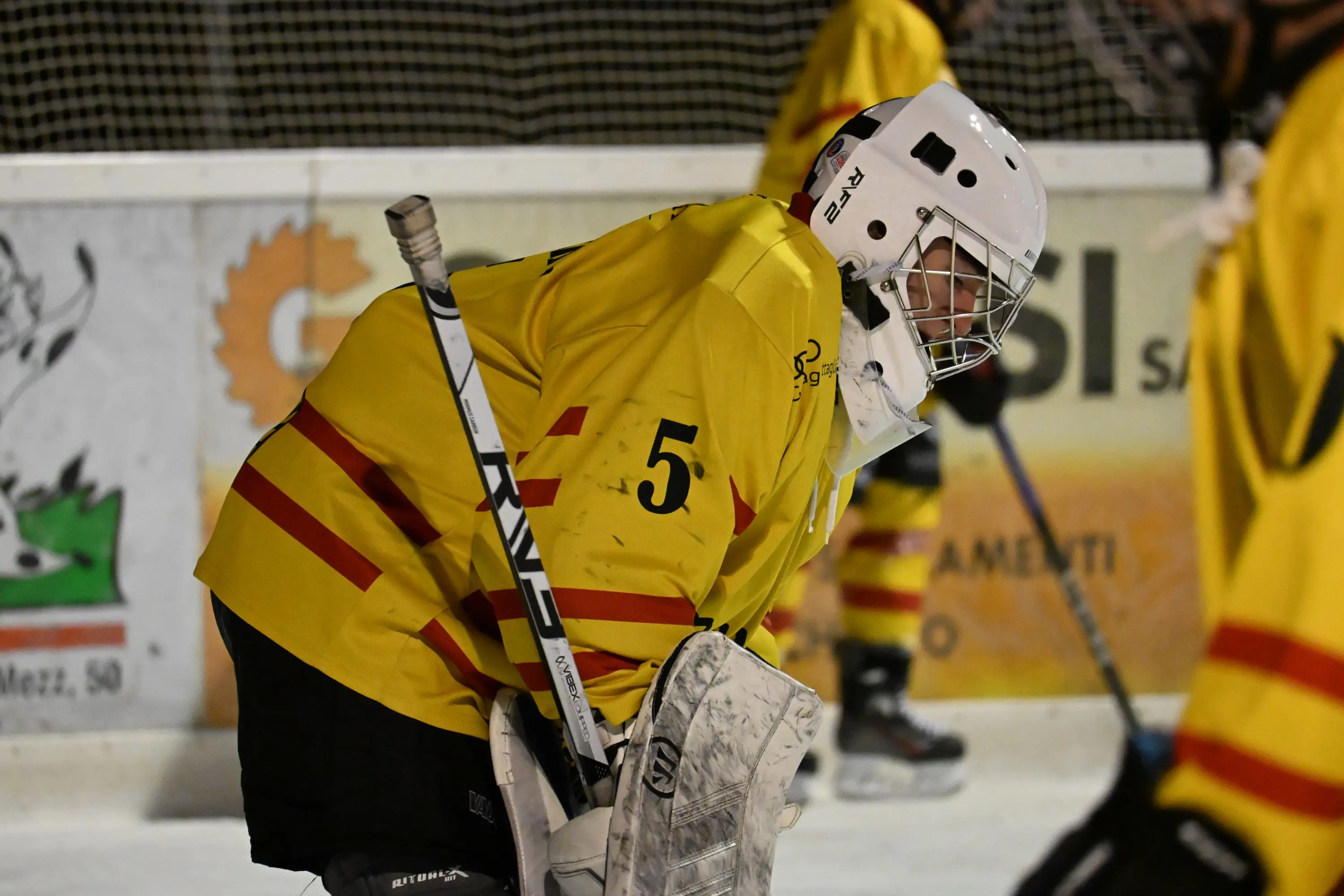 Giocatore di hockey su ghiaccio in uniforme gialla con casco bianco e guanti, piegato in avanti mentre si prepara per il gioco.