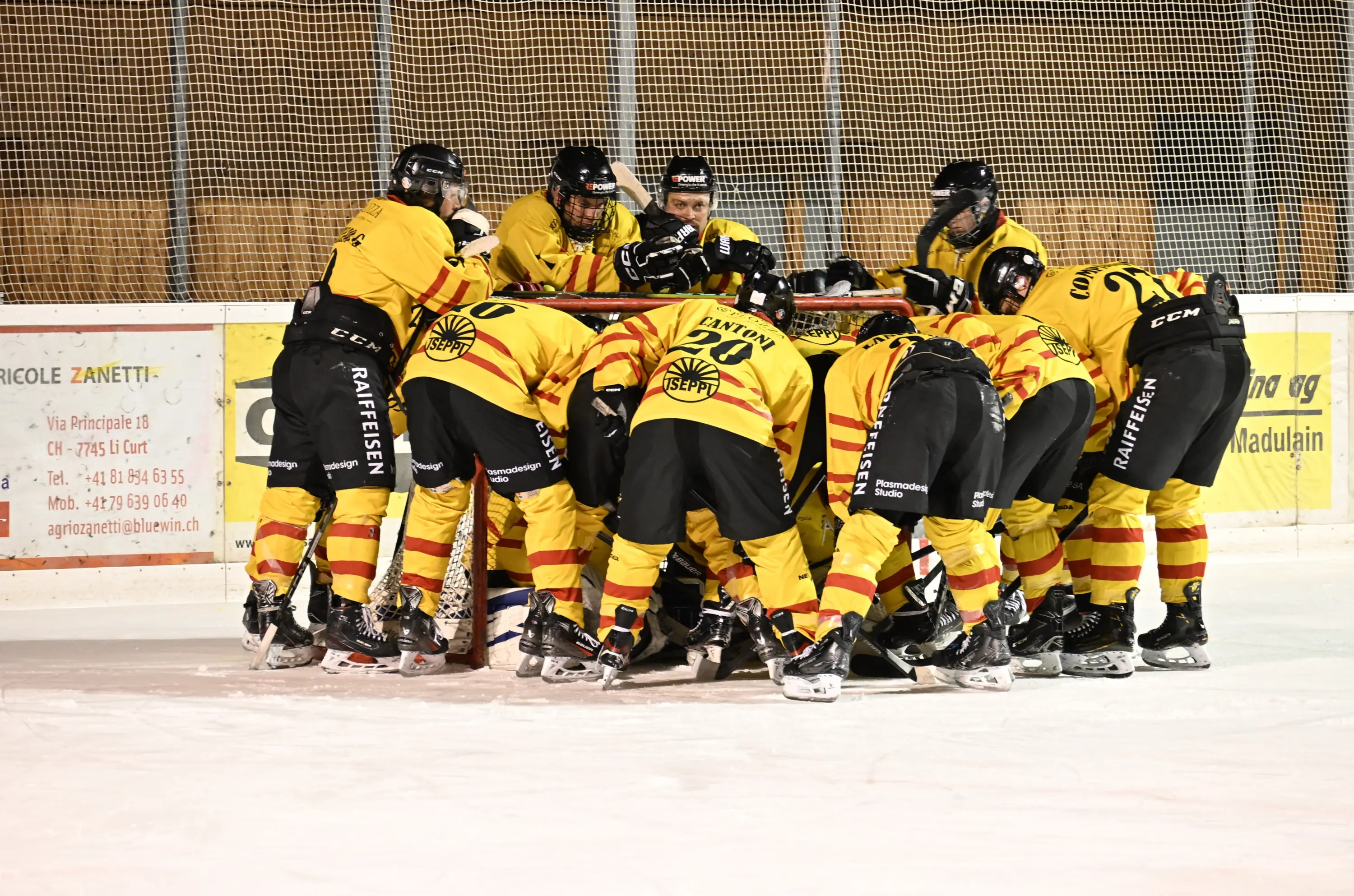 Giocatori di hockey su ghiaccio in un momento di team building, riuniti in cerchio con divise gialle e nere. L'atmosfera è di concentrazione e spir