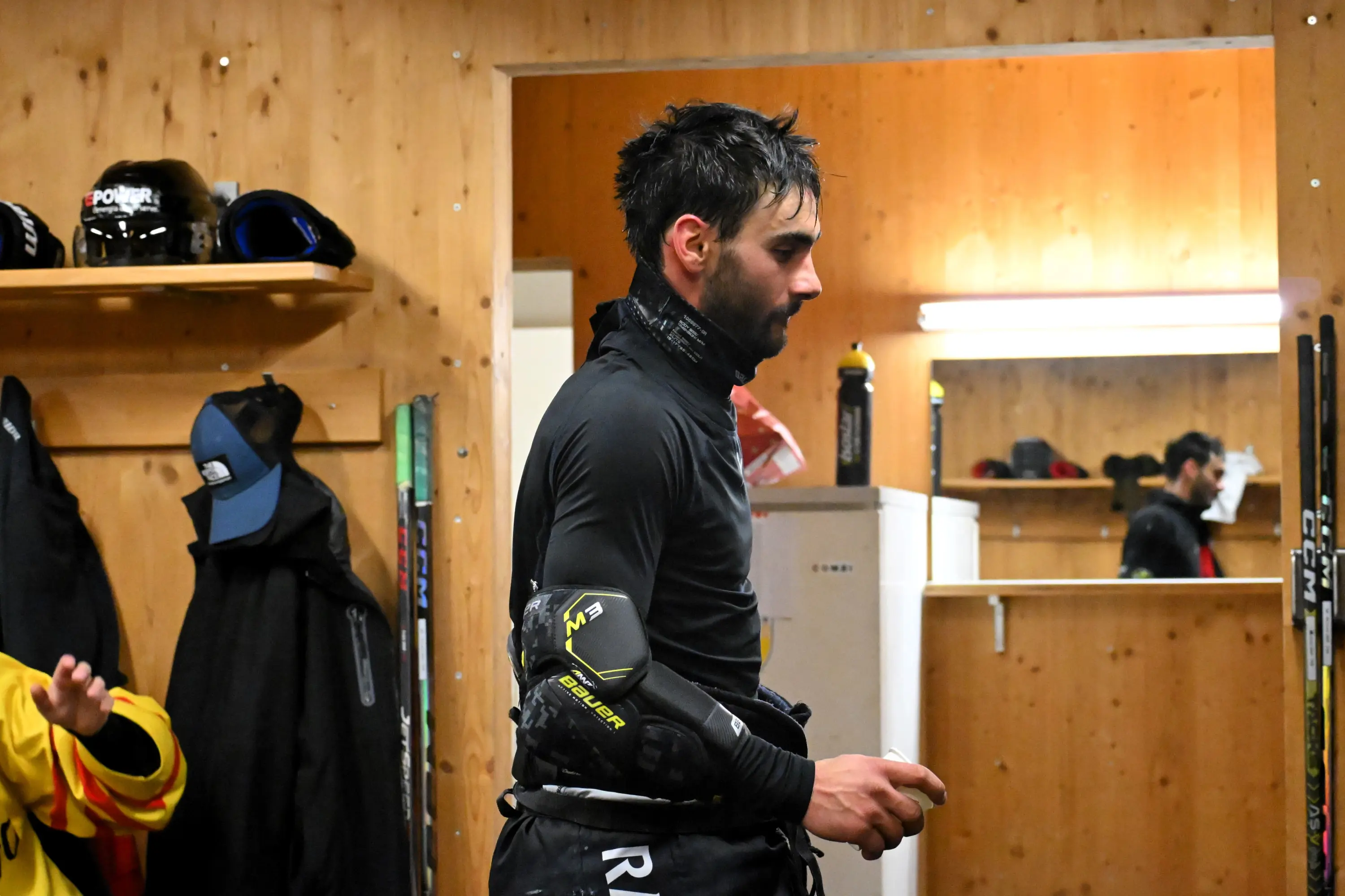 Giocatore di hockey su ghiaccio in abbigliamento sportivo, si trova in uno spogliatoio con pareti di legno. Ha i capelli bagnati e indossa