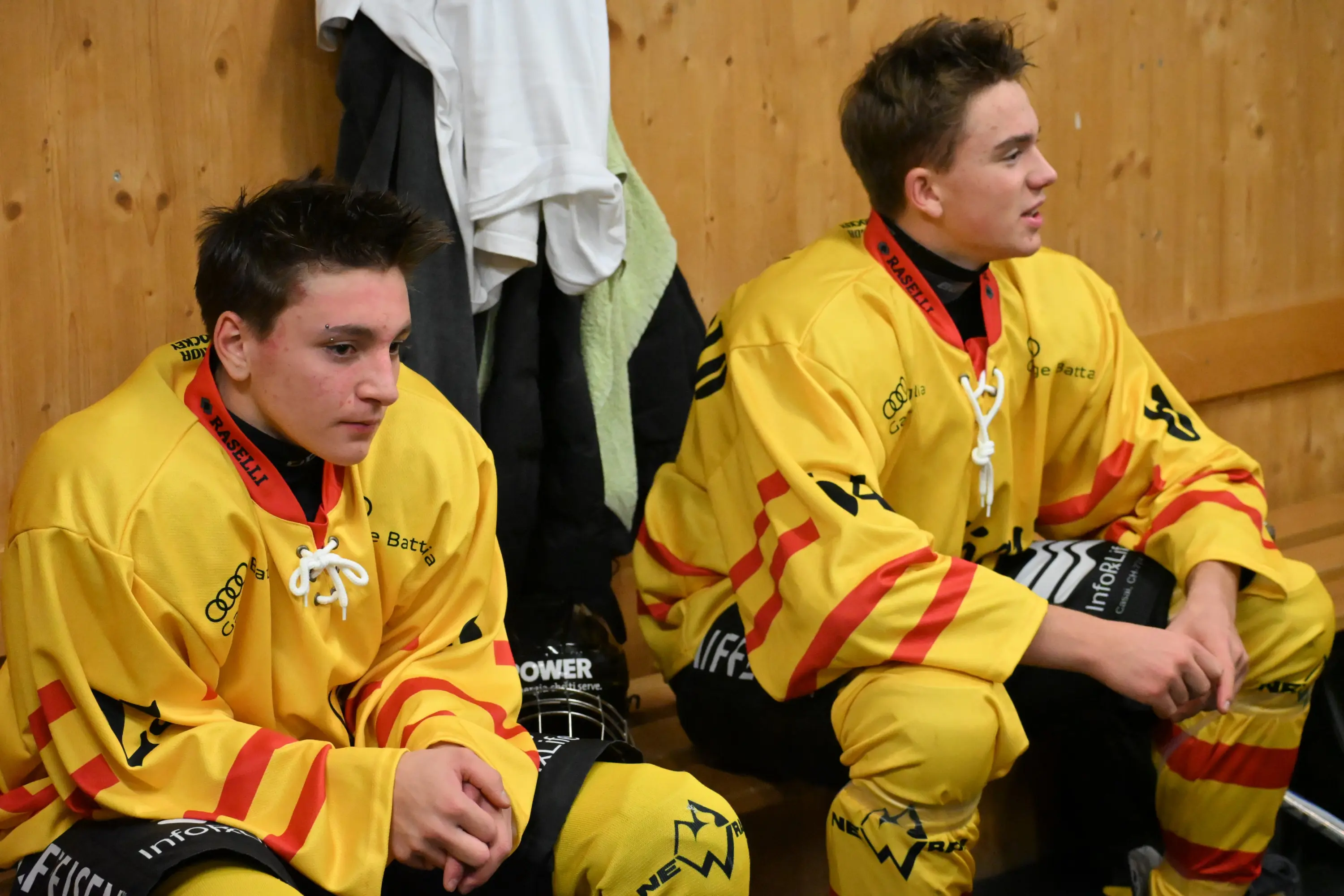 Giocatori di hockey su ghiaccio seduti in uno spogliatoio, indossando uniformi gialle con strisce rosse. Sembri meditando prima della partita,