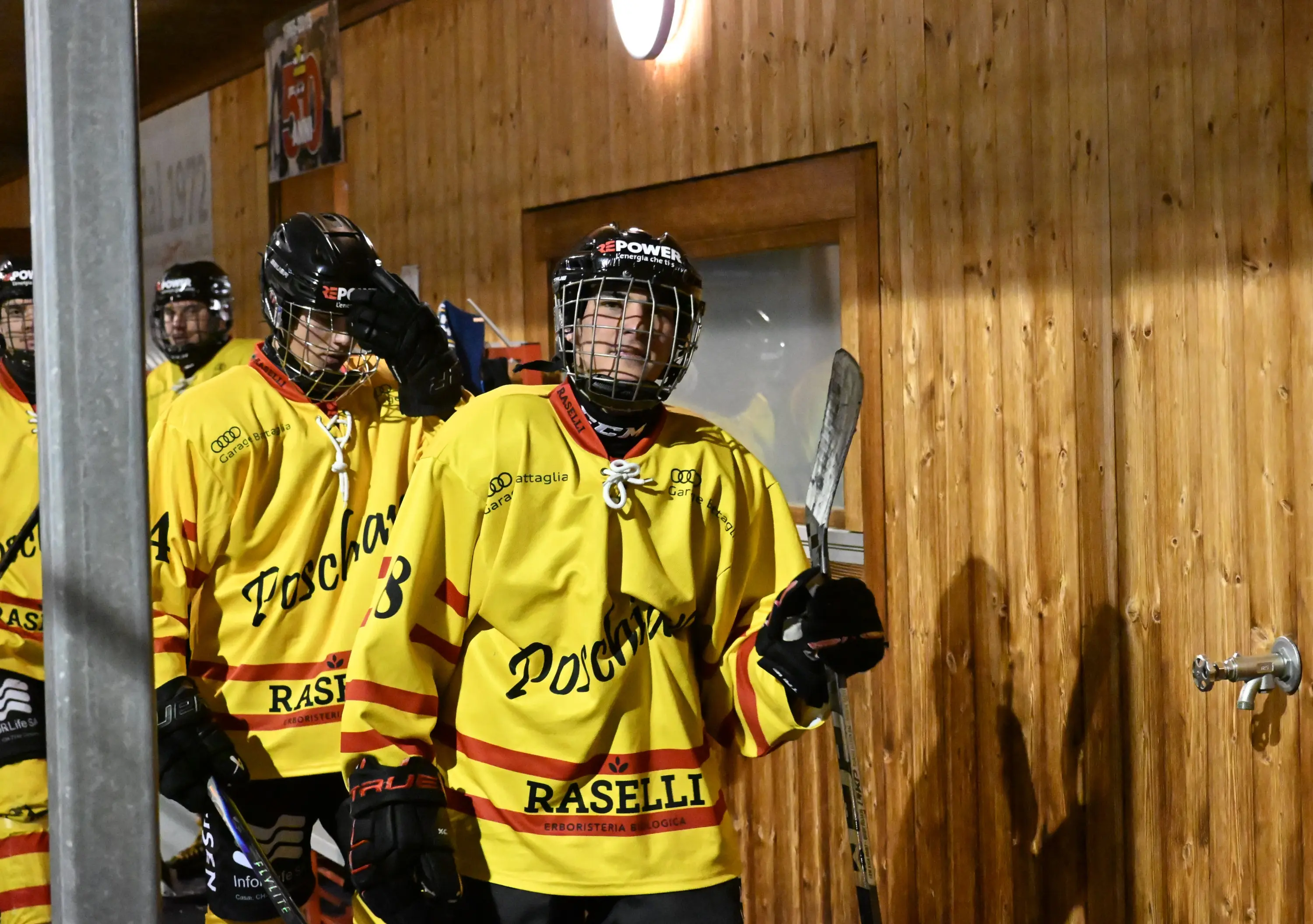 Giocatori di hockey su ghiaccio indossano maglie gialle e neri mentre si preparano per entrare in campo. L'ambiente è un palazzetto sportivo in