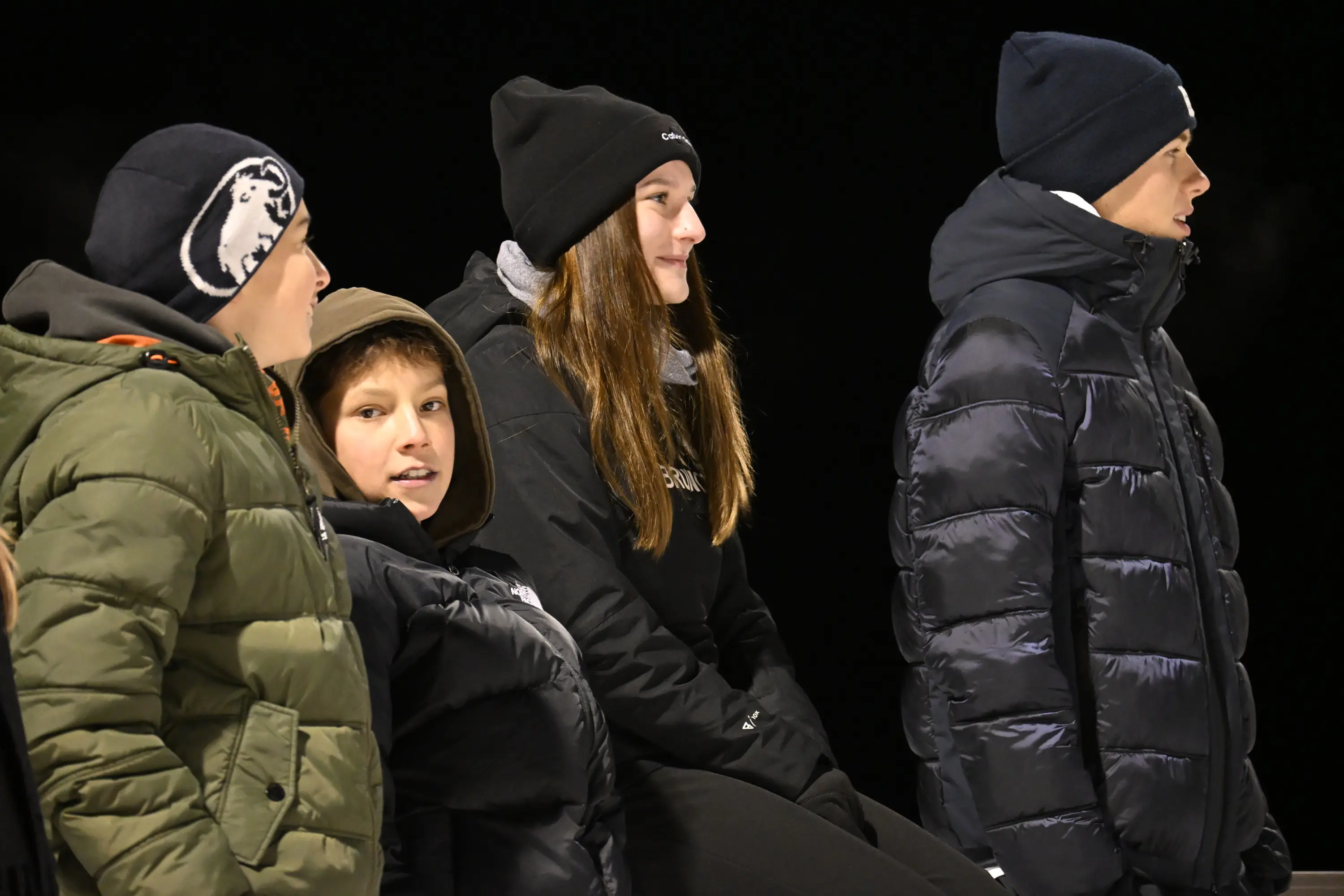 Gruppo di giovani in abbigliamento invernale seduti insieme all'aperto, con espressioni concentrate e sorridenti, durante un'attività notturna.