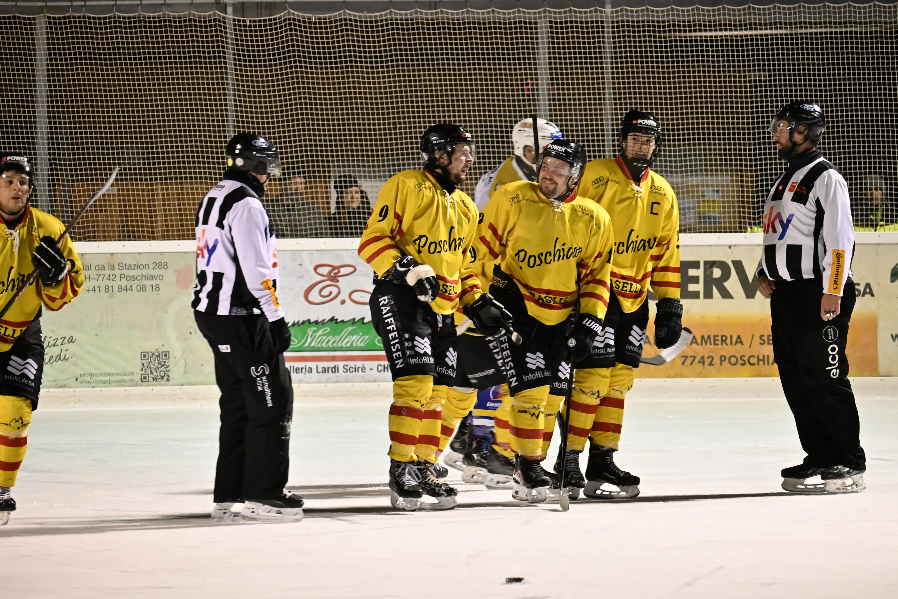 Giocatori di hockey su ghiaccio in maglia gialla e rossa si riuniscono sul ghiaccio, mentre l'arbitro in maglia a strisce bianche e nere