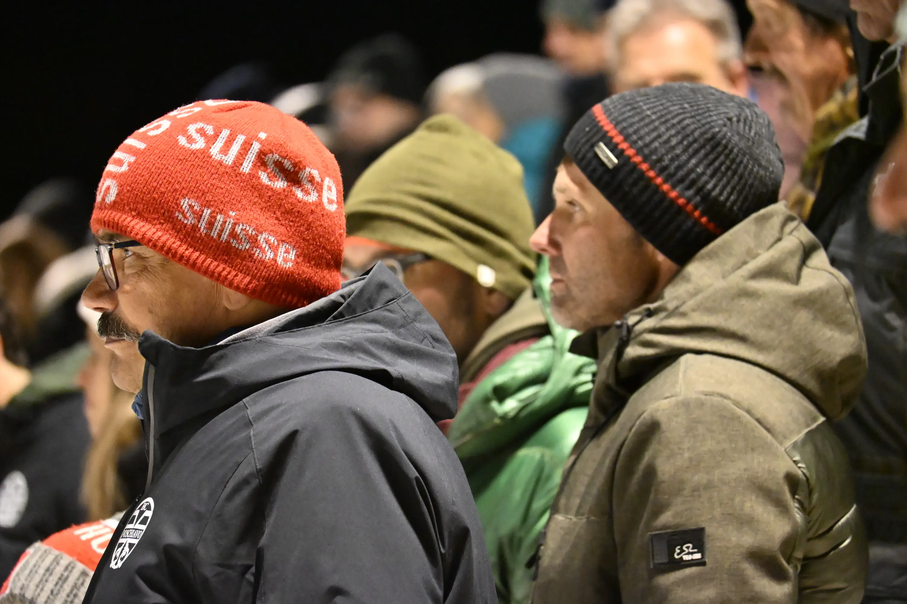 Tifosi in prima fila, indossando berretti e giacche invernali, mentre guardano un evento sportivo. L'atmosfera è vivace e coinvolgente.