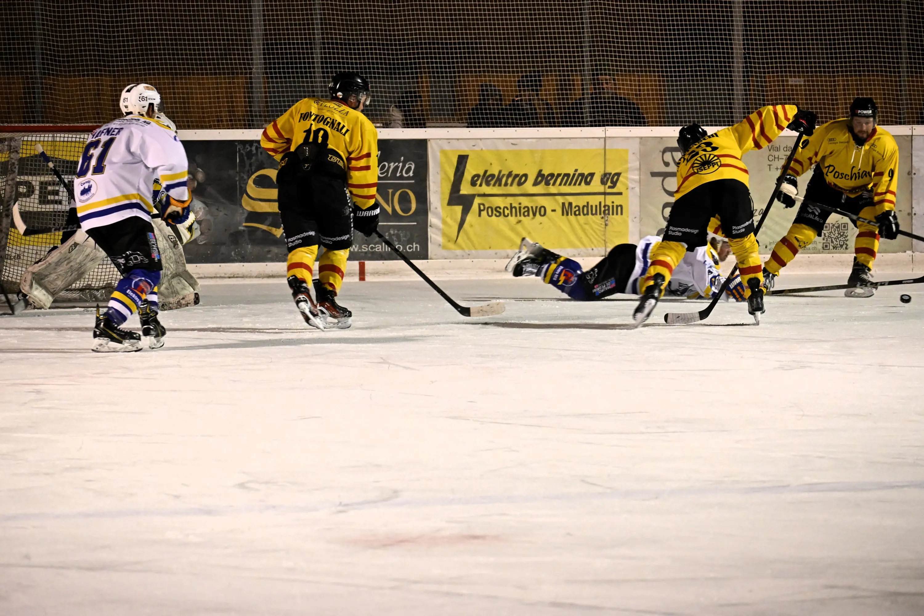 Giocatori di hockey su ghiaccio in azione durante una partita. Due delle squadre indossano maglie gialle e nere, mentre un giocatore in maglia bianca è
