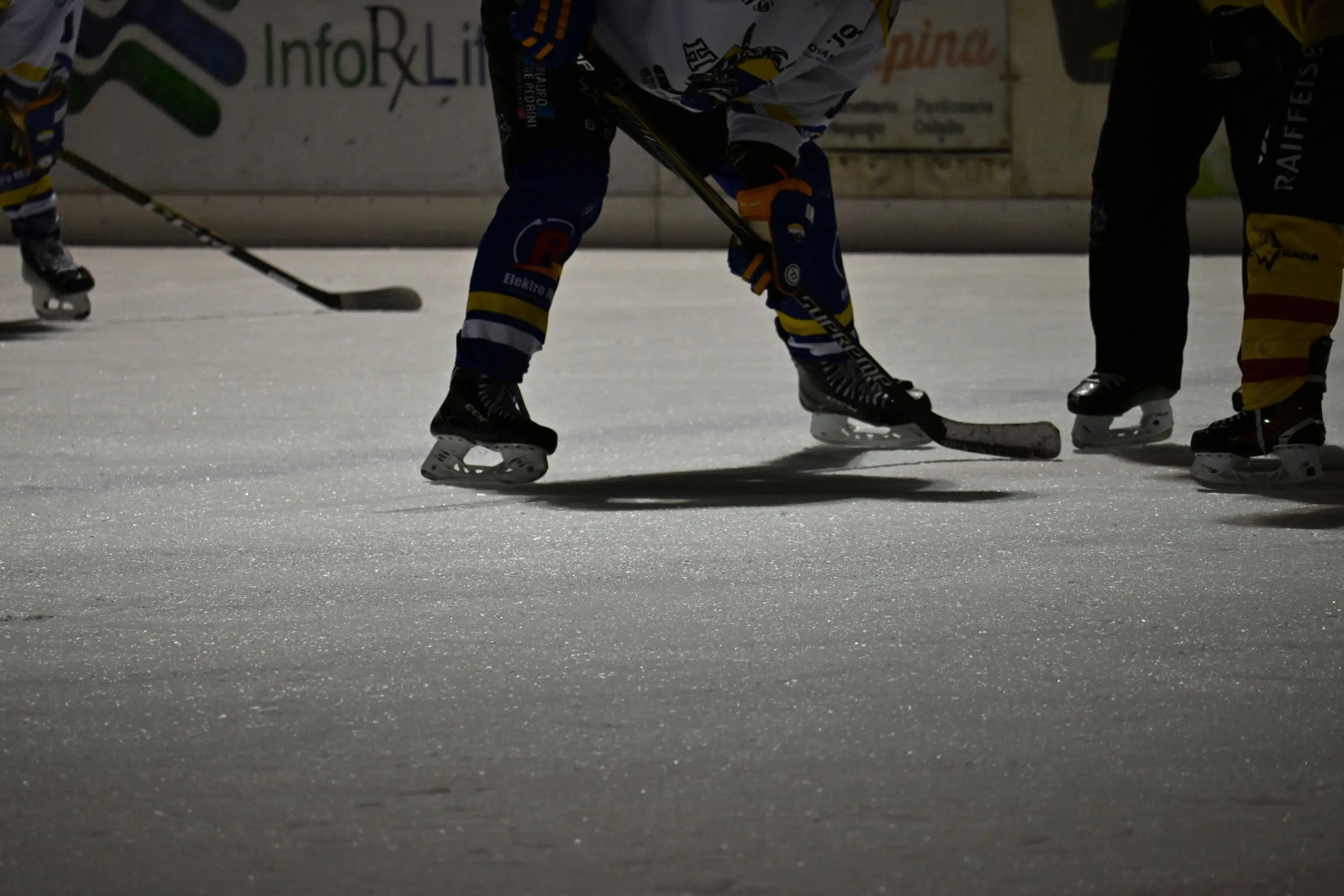 Giocatori di hockey su ghiaccio che si preparano a ingaggiare, con pattini e bastoni in evidenza su una superficie ghiacciata.